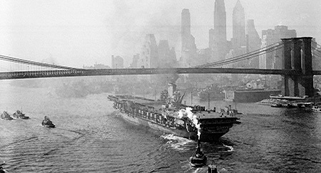 The aircraft carrier USS Franklin D. Roosevelt sails down the East River under the Brooklyn Bridge in New York City, 1945. The carrier is leaving the Brooklyn Navy Yard for the Navy Yard annex in Bayonne, N.J., where it will undergo further conditioning.