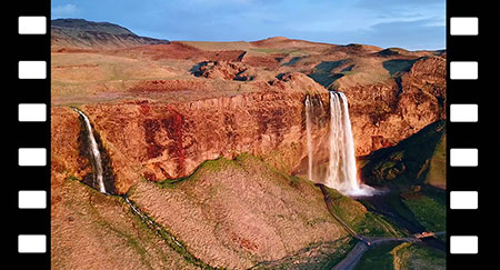 Aerial drone shot overlooking the Seljalandsfoss waterfall and the Seljalands river, at golden hour, in Iceland