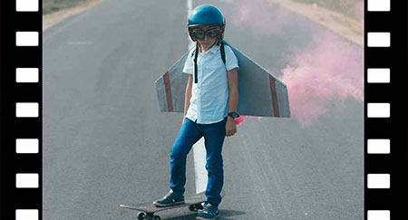Cinemagraph eines kleines Jungen mit Styroporflügeln, der auf einem Skateboard steht