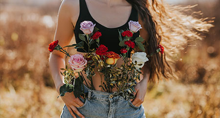 Giovane donna in jeans dai capelli lunghi nella natura, fiori di vario genere, concept di benessere femminile.