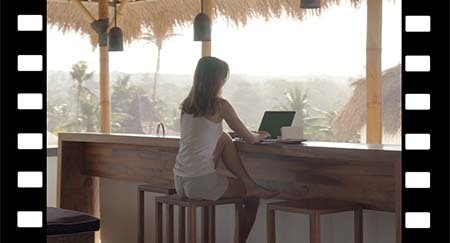 Frau arbeitet am Laptop und schreibt in einen Notizblock auf exotischer Terrasse