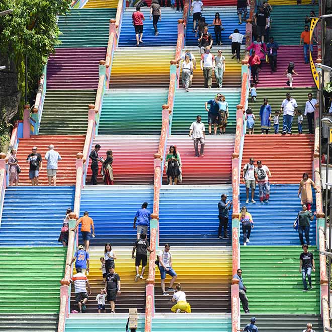 Tourists climbing a colourful stairs leading to the Batu Caves. 