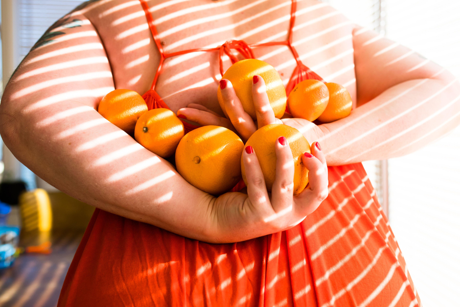 Femme portant une robe orange tenant sept oranges derrière son dos