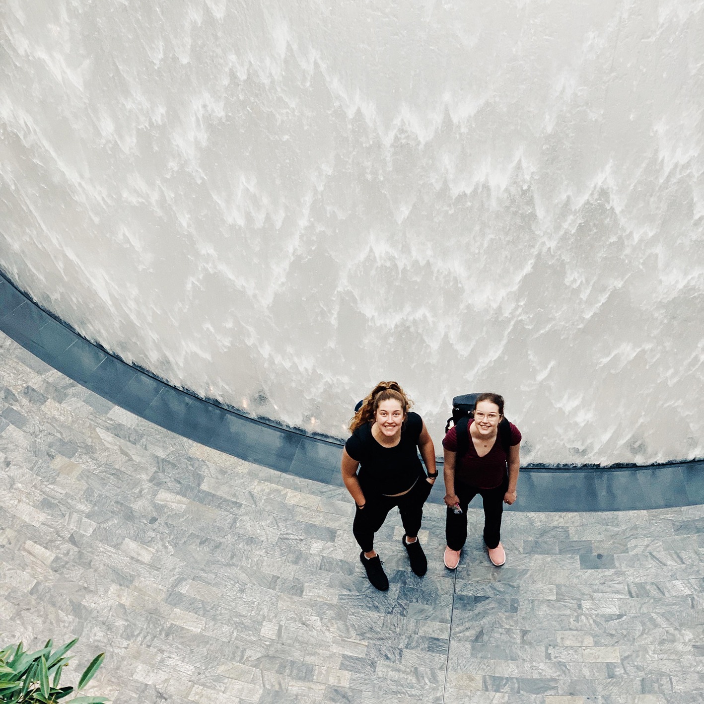 Two young women looking up in front of waterfall at Jewel in Changi Airport, Singapore