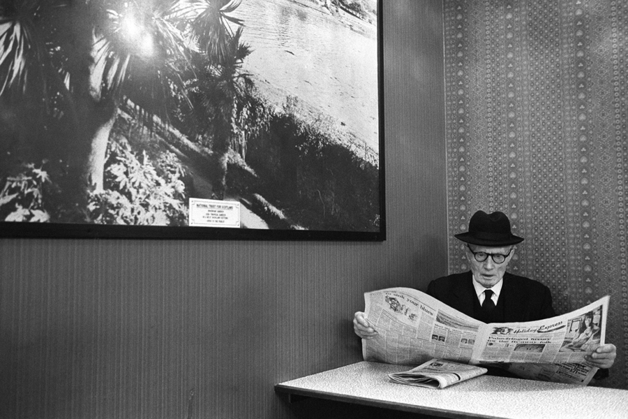 Older man looking surprised while reading the the Holiday Express section of the Daily Express newspaper. London, England, 1975.