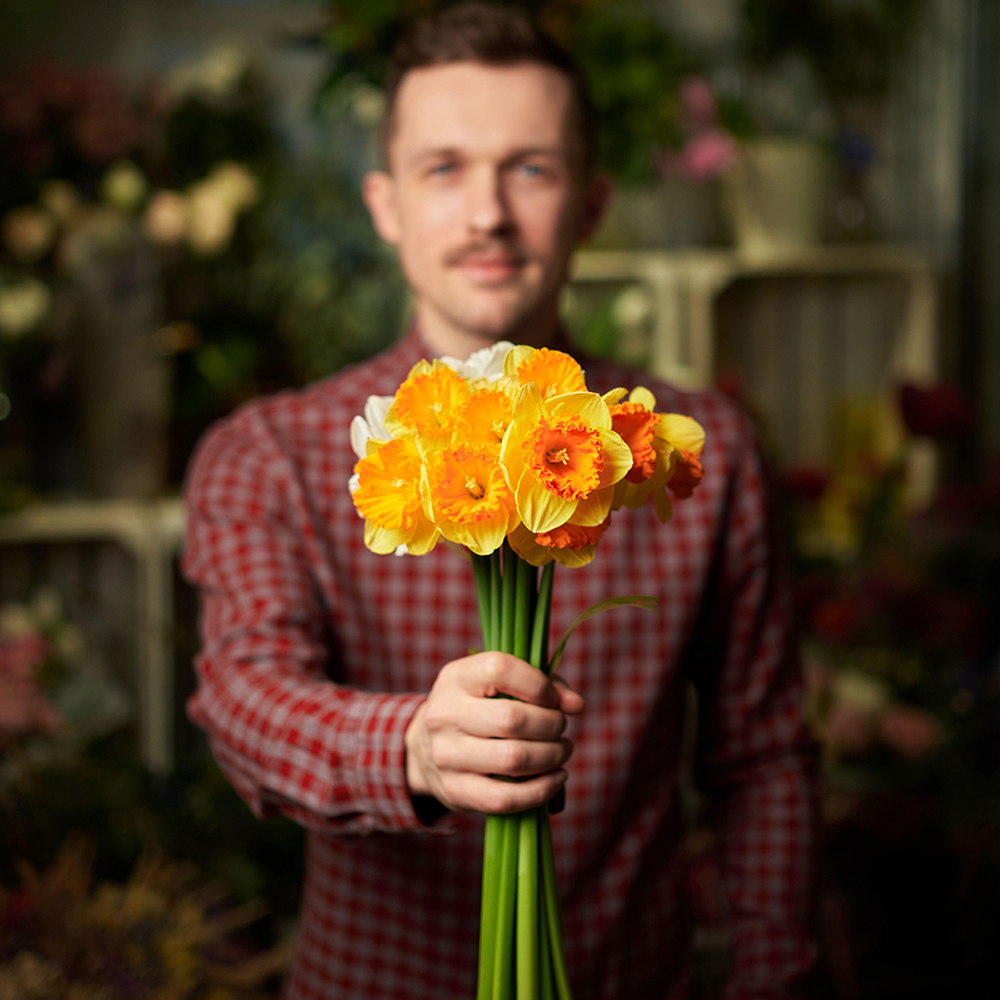 Congratulating with flowers: man in shirt holding beautiful bouquet of yellow and orange fresh spring flowers