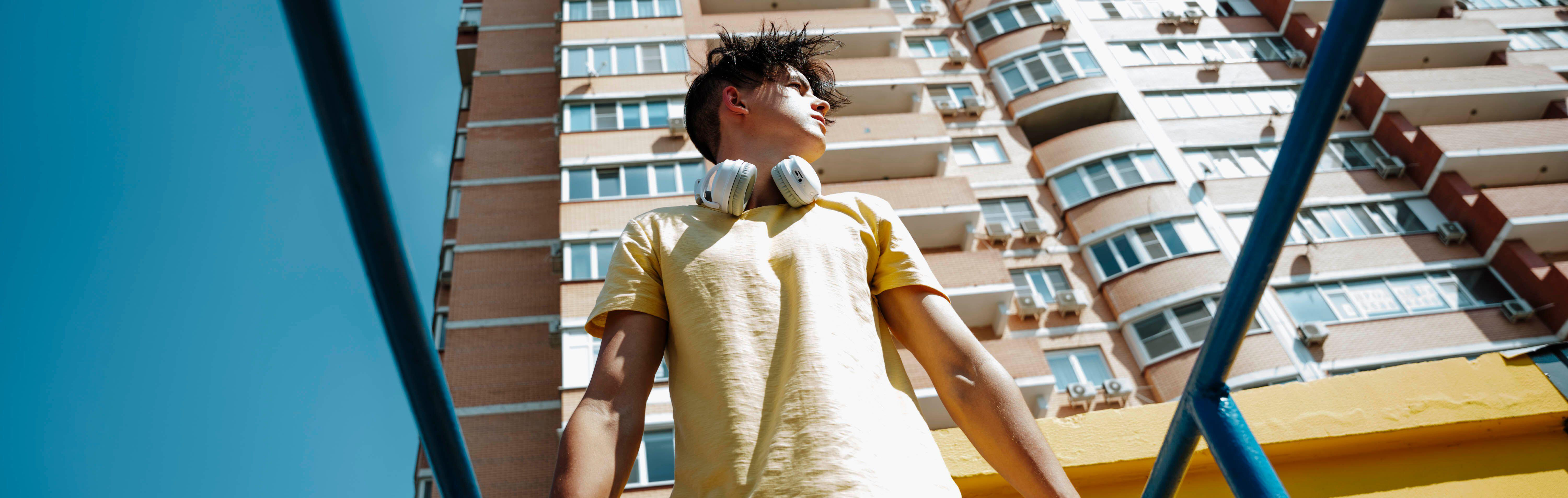 Young man with wireless headphones standing near bars in front of building