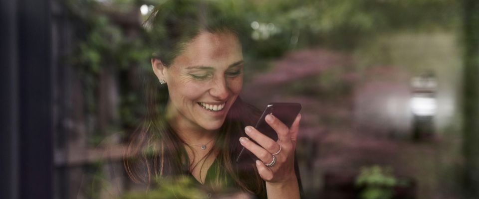 Smiling mid adult woman using mobile phone at home seen through window. 