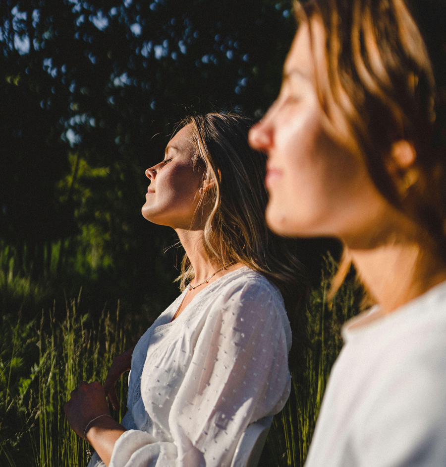 Young woman with eyes closed sitting by friend enjoying sunlight