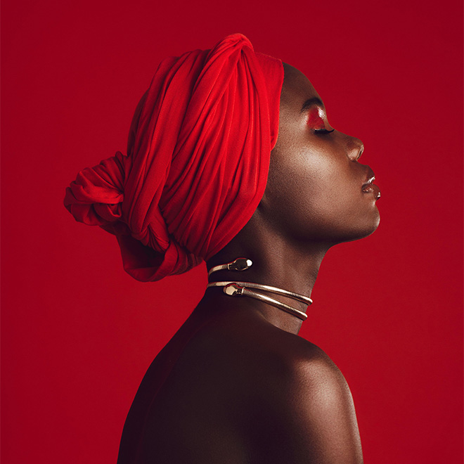 Seitenansicht einer Frau mit rotem Turban im Studio. Stilvolles weibliches Model mit geschlossenen Augen vor rotem Hintergrund.