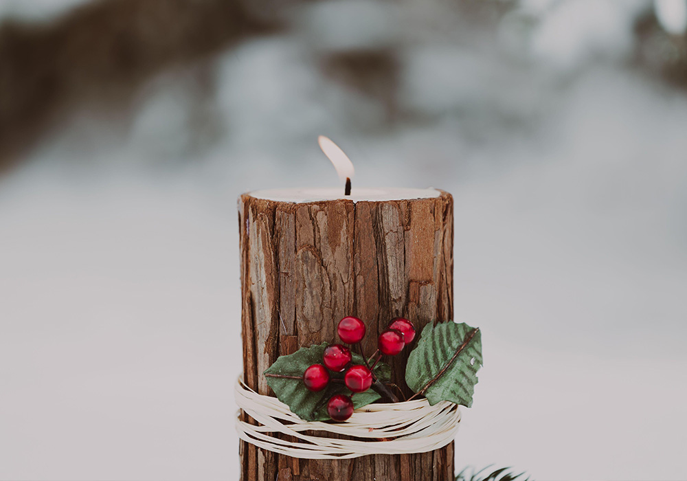 Christmas candle lit with rustic bark wrap and twine and red berries with evergreen wreath base in the snow outdoors in the winter with copy space 