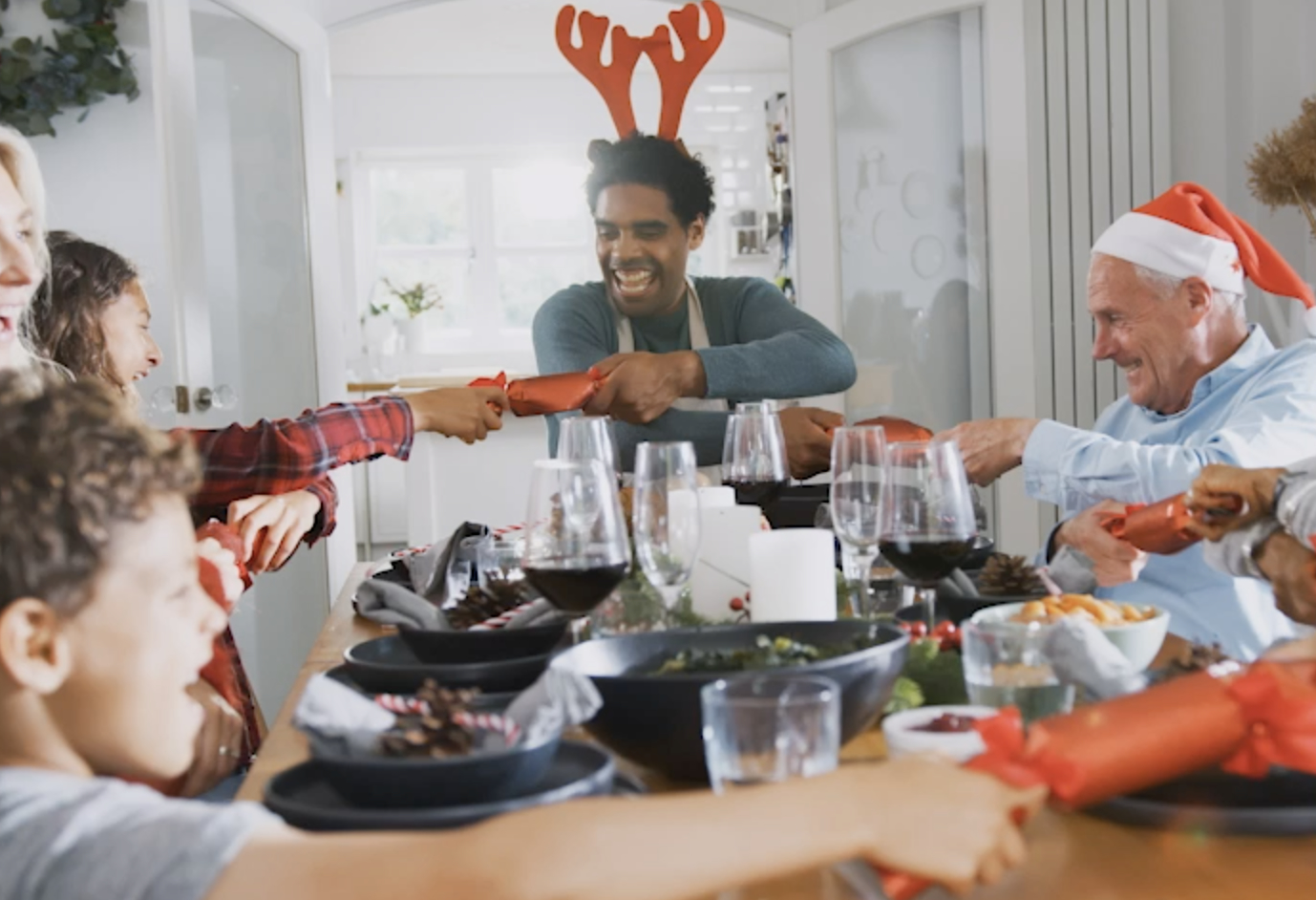 Multigenerationelle Familie zieht Weihnachtsknallbonbons, während sie am Tisch zum Essen sitzt.