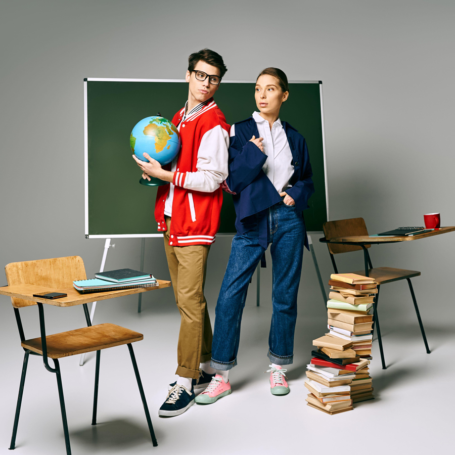Two students posing in front of a green board with a globe in a college classroom