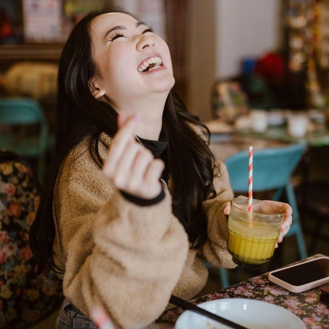 Young woman laughing while holding drink sitting at restaurant - Image ID: 2NRF3MB (RF) enterprise 