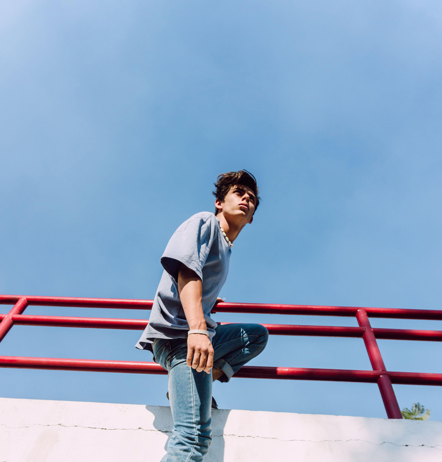 From below side view of of brave male hanging looking away over metal fence in street and showing parkour trick against blue sky