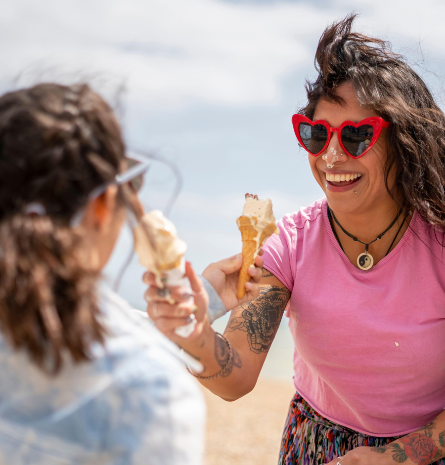 Eine lächelnde Mutter und ihre Tochter essen am Strand ein Eis