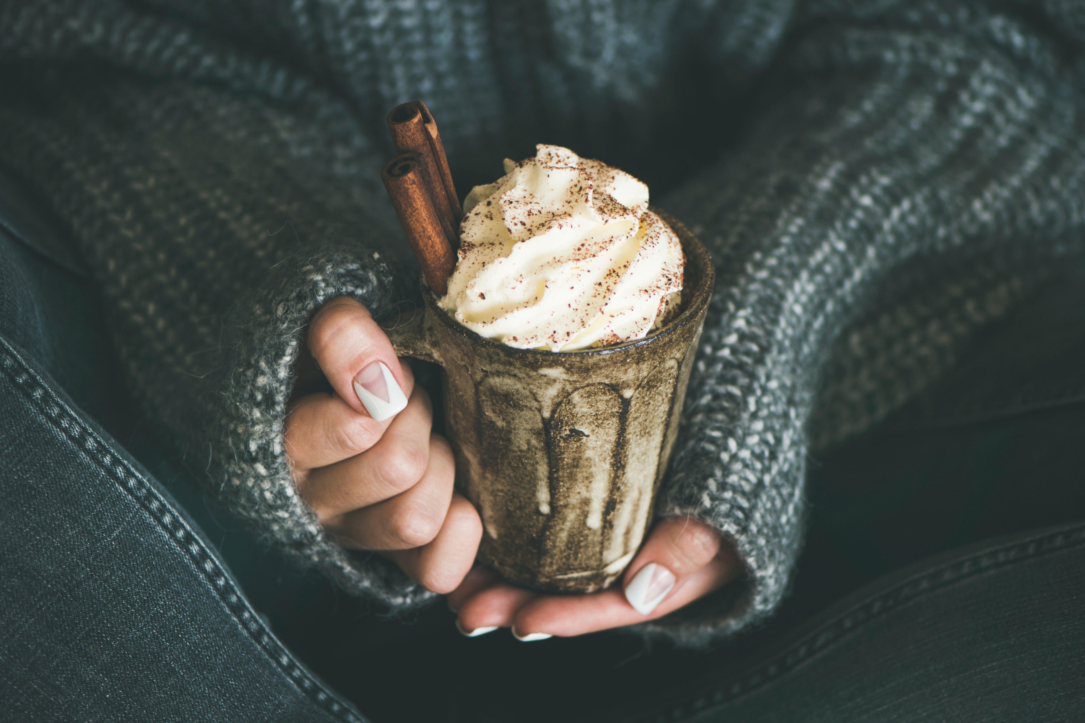 Woman holding mug with hot chocolate with whipped cream and cinnamon