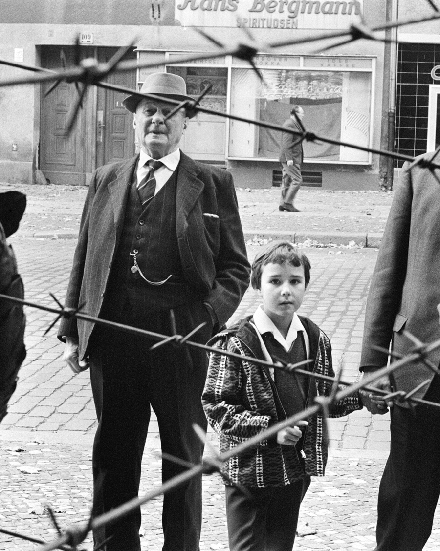 Scenes in Berlin, three years after work began on the construction of the Berlin Wall, separating East from West. Citizens of Berlin peer through the barbed wire fence to their neighbours on the other side. 25th October 1964