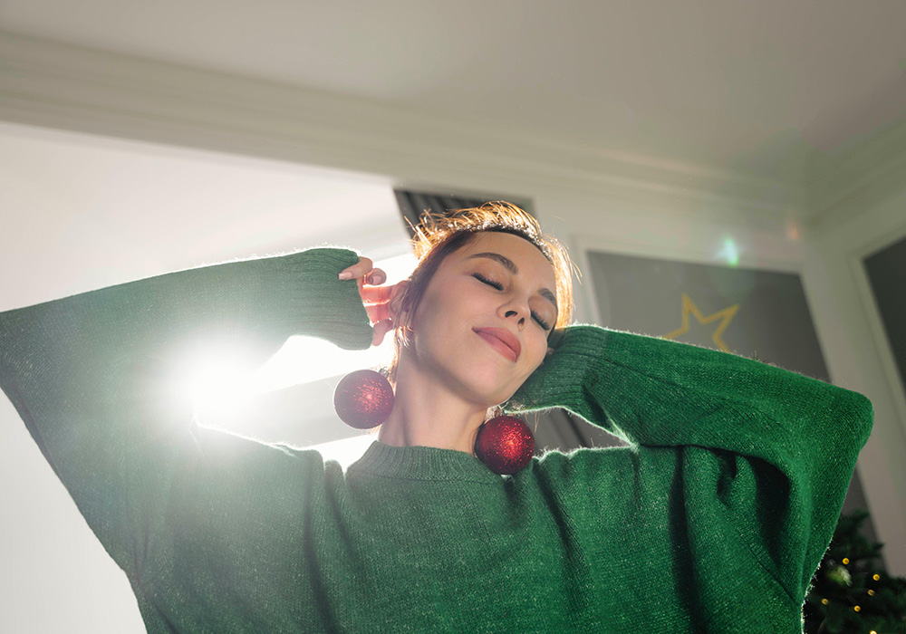 Smiling woman holding Christmas ornaments by ears at home