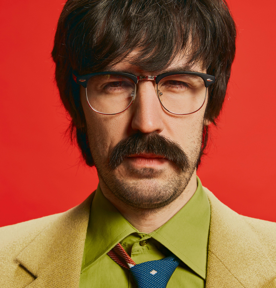 Ritratto ravvicinato di un uomo elegante con i baffi in posa con un abito vintage, isolato su sfondo rosso.