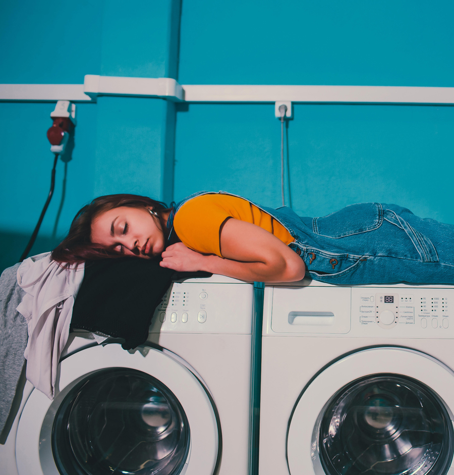 Young woman searching clothes in washing machine drum at laundromat