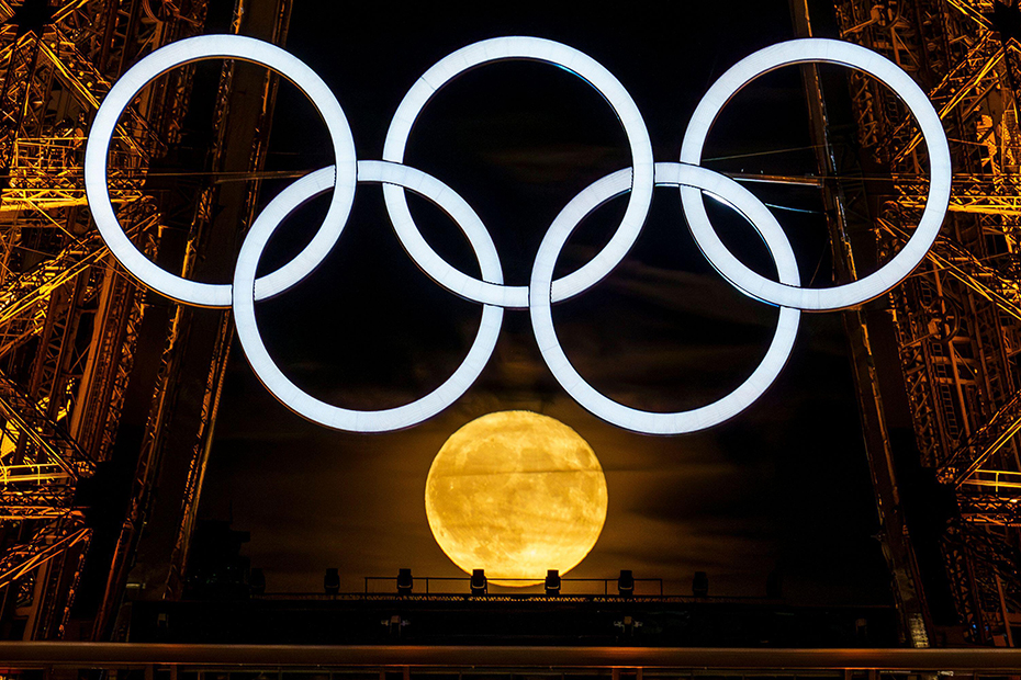 La luna piena sorge dietro i cerchi olimpici sulla Torre Eiffel mentre la città si prepara ad ospitare i Giochi estivi del 2024 a Parigi, in Francia.
