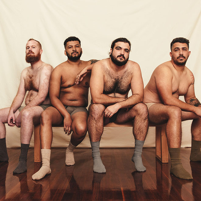 Group of body positive men looking at the camera while sitting shirtless on a studio bench. Self-confident young men wearing underwear. Four young men.