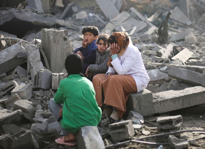 Palestinesi sono seduti accanto alla distruzione causata dai bombardamenti israeliani nella Striscia di Gaza a Rafah lunedì 12 febbraio 2024.