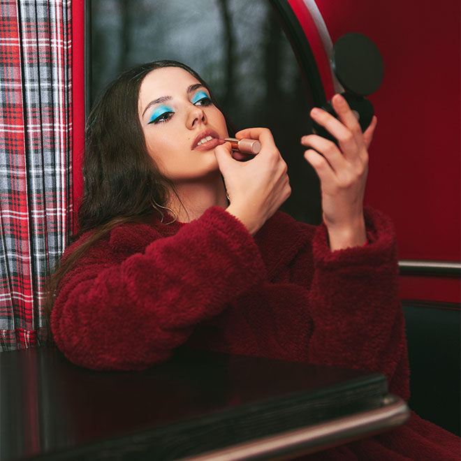 Attractive girl sitting in the cafe bus (bistro) and painting her lips by lipstick. Retro (vintage) portrait of beautiful stylish young woman in resta