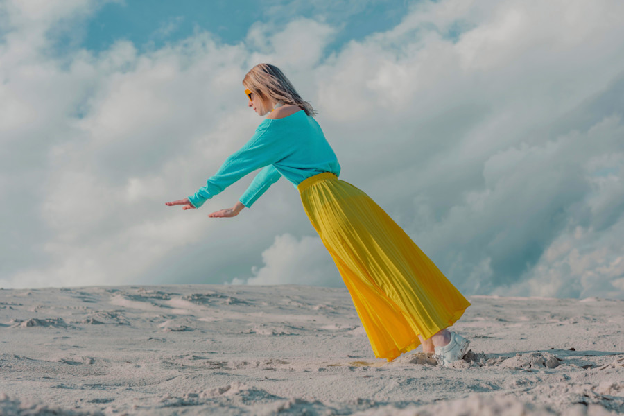 Woman wearing yellow skirt balancing on toes under cloudy sky