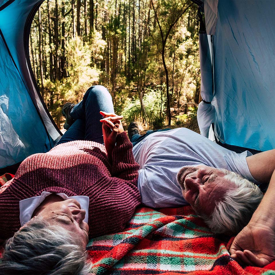 2BH8EHN- Coppia di anziani riposa sdraiata all'interno di una tenda in campeggio libero nella foresta per viaggi e stili di vita alternativi. 