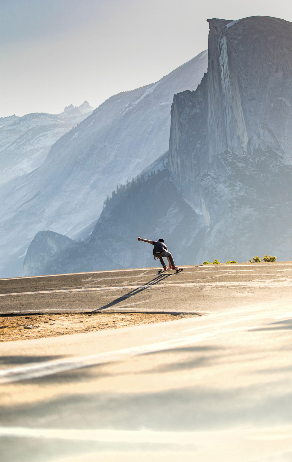 A vertical shot of a person riding a skate on the edge of a cliff with mountains in the background
