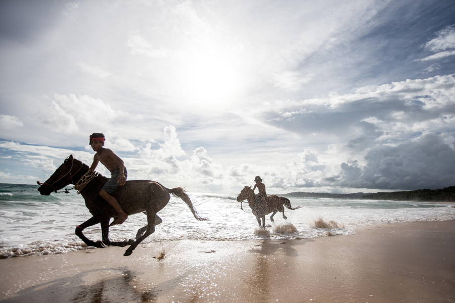 Zwei kleine Jungen spielen mit ihren Pferden am Meer in Nihiwatu, Sumba, Indonesien, Südostasien, Asien