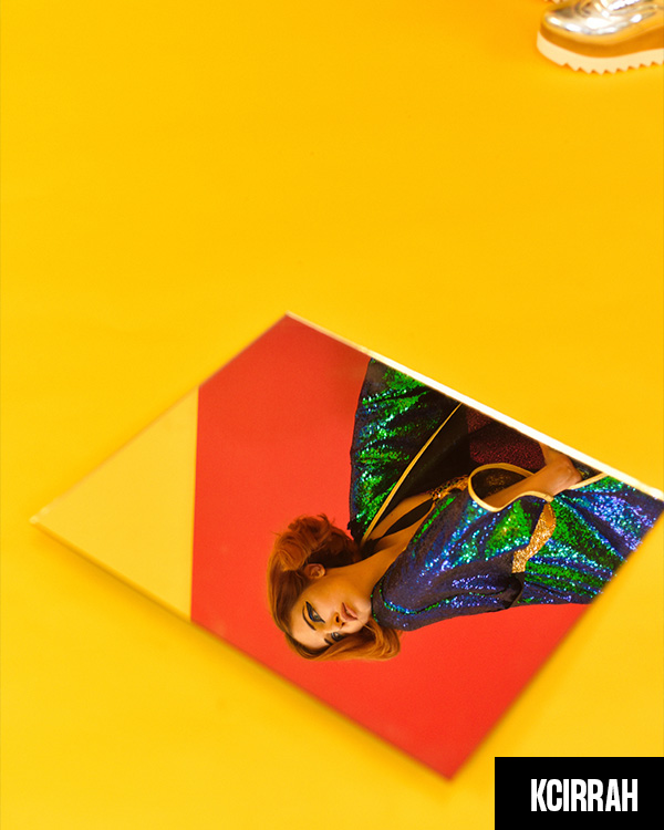 A beautiful redhead in bright festival clothing is in a studio set up with red and yellow background- fun fashion shoot