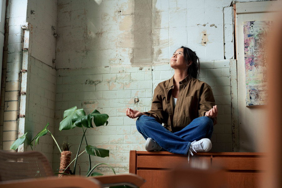 Smiling painter sitting cross-legged on cabinet by paintings at art studio