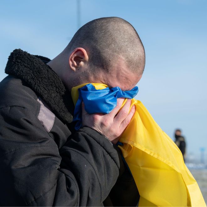 A Ukrainian soldier weeps into a Ukraine flag after arriving back home following a POW exchange between Russia and Ukraine, January 31, 2024 