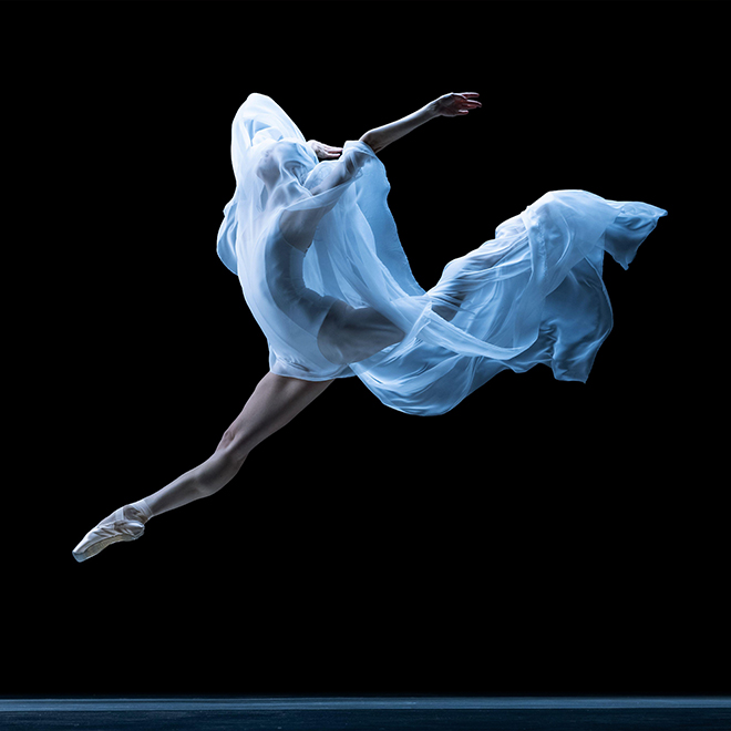 Anmutige klassische Ballerina tanzt mit schwerelosem Stoff vor schwarzem Studiohintergrund im Neonlicht.