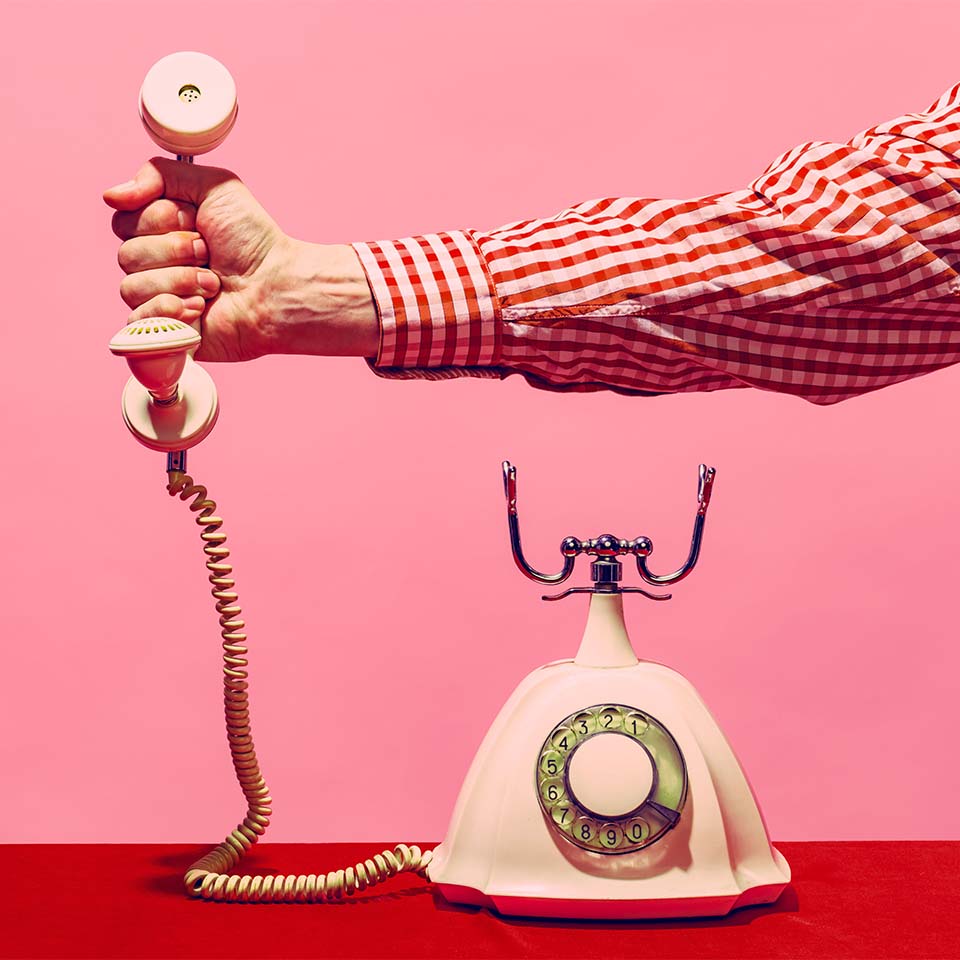 Fotografia pop art. Oggetti retrò, gadget. Mano femminile che tiene la cornetta di un telefono vintage su sfondo rosa e rosso. Moda vintage e retrò.
