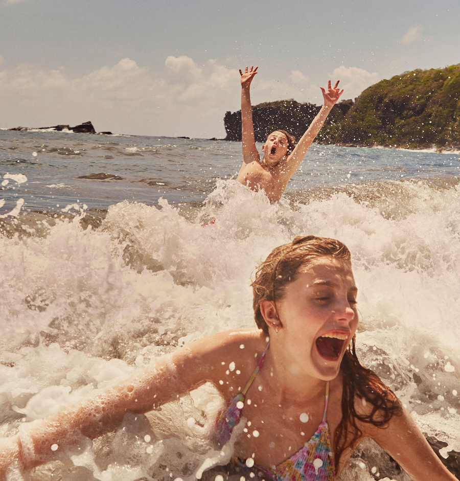 Happy, carefree boy and girl swimming and splashing in sunny ocean waves, Kingstown