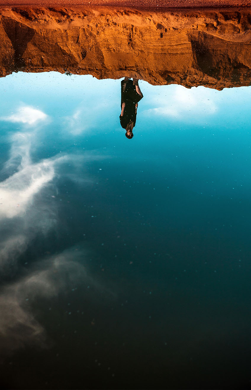 JB1PH9 - Une femme debout sur le sable et son reflet dans l’eau. Oasis dans le désert