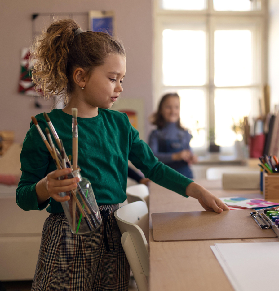 Une petite fille heureuse avec ses amis se prépare pour un cours d'art et d'artisanat à l'intérieur de l'école