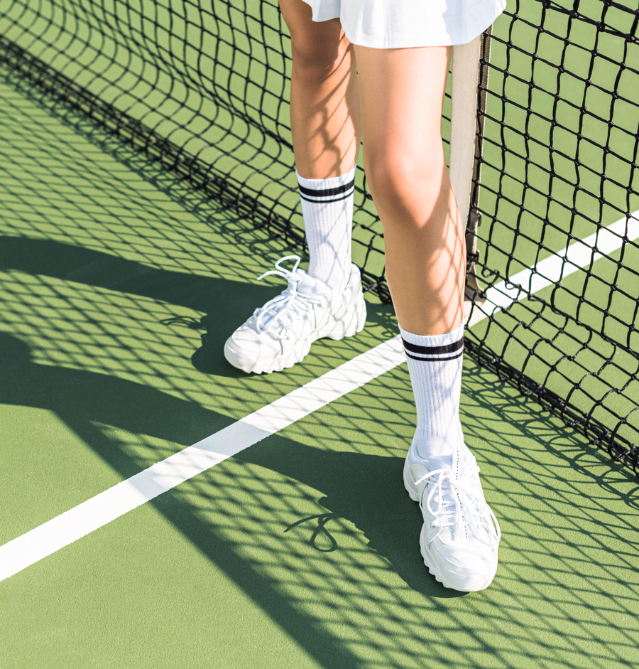 Gros plan créatif des jambes et des pieds d'une joueuse de tennis debout près du filet sur le court