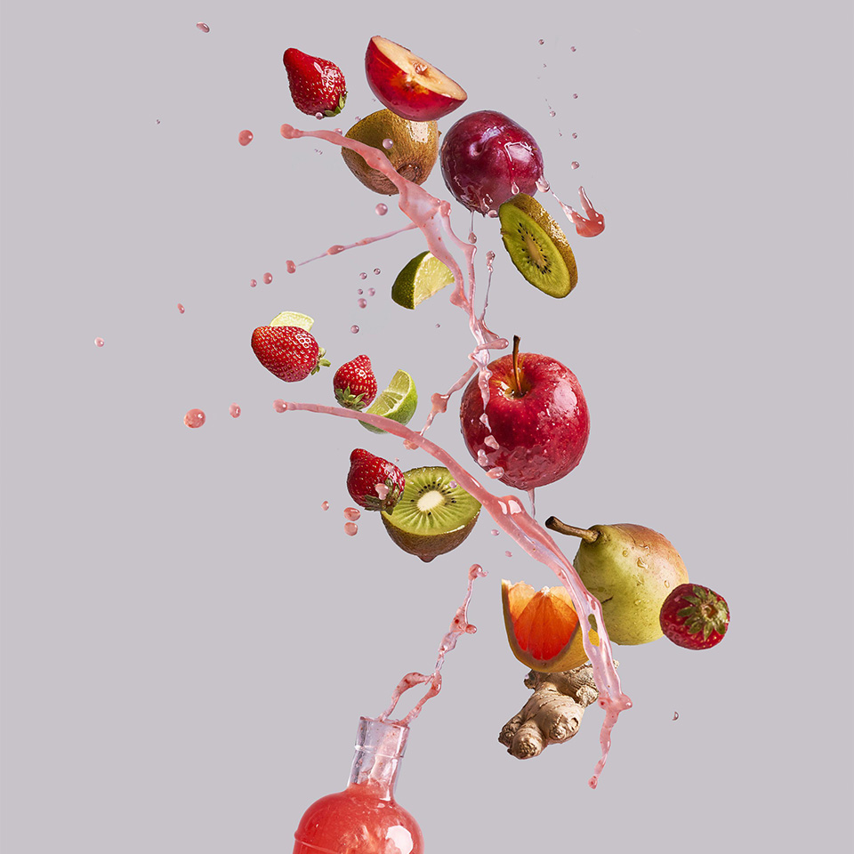 Bunch of various fresh fruits and ginger falling into glass bottle with healthy juice against gray background 