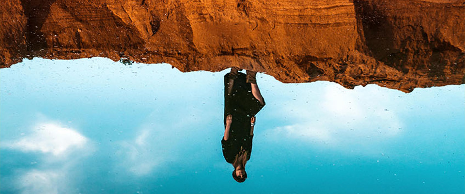 A woman standing on the sand and her reflection in the water. Oasis in the desert