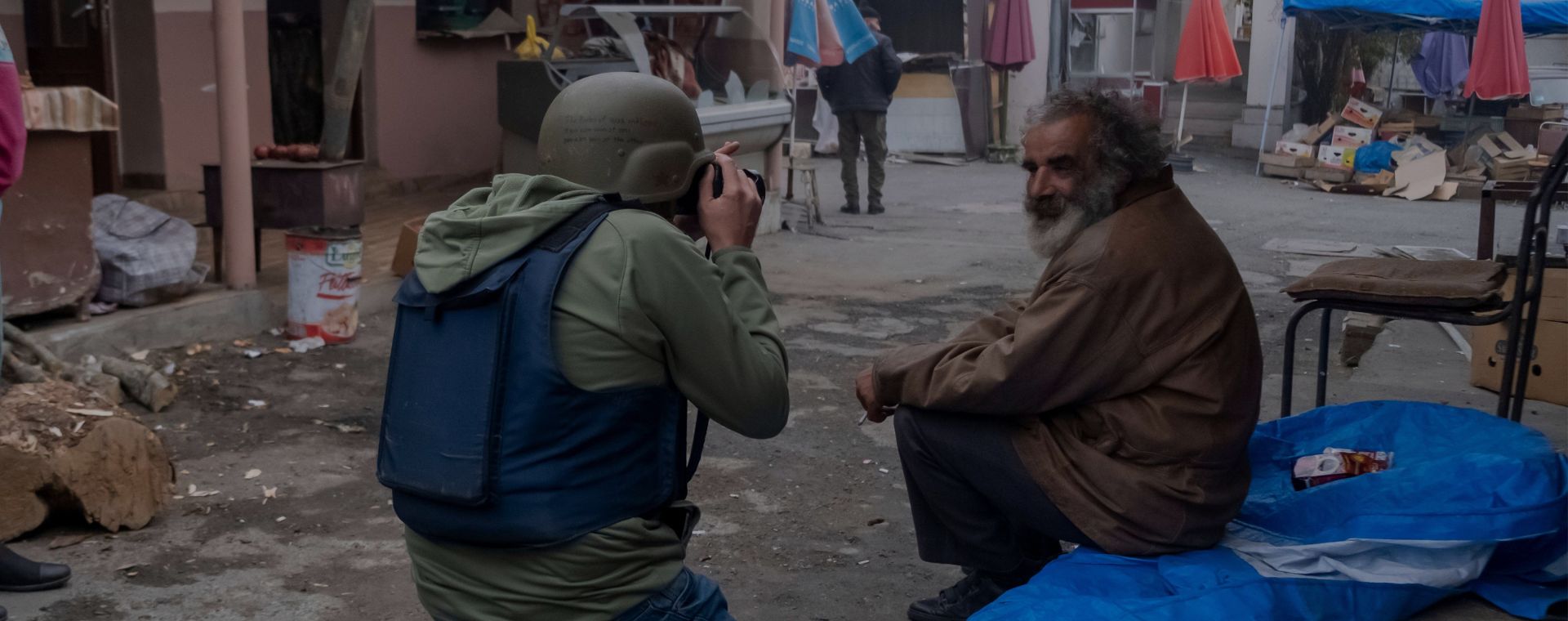 Un fotografo indossa una giacca antiproiettile protettiva e un casco fotografando un anziano locale durante un conflitto militare tra le forze armene e azere al mercato centrale di Stepanakert.