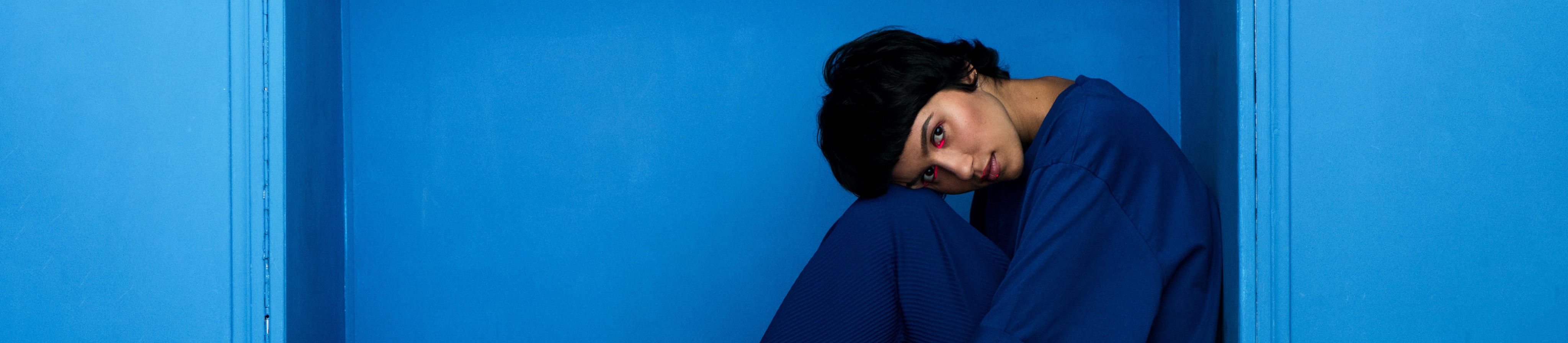 Young beautiful woman sitting in niche on blue background. Studio shot. - Image ID: 2A95J64 (RF)