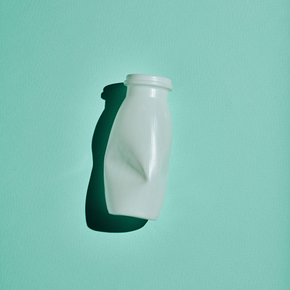 Prise de vue minimaliste à plat verticale d'une bouteille en plastique blanche sur un fond vert bleuté, concept de consommation consciente et de recyclage.