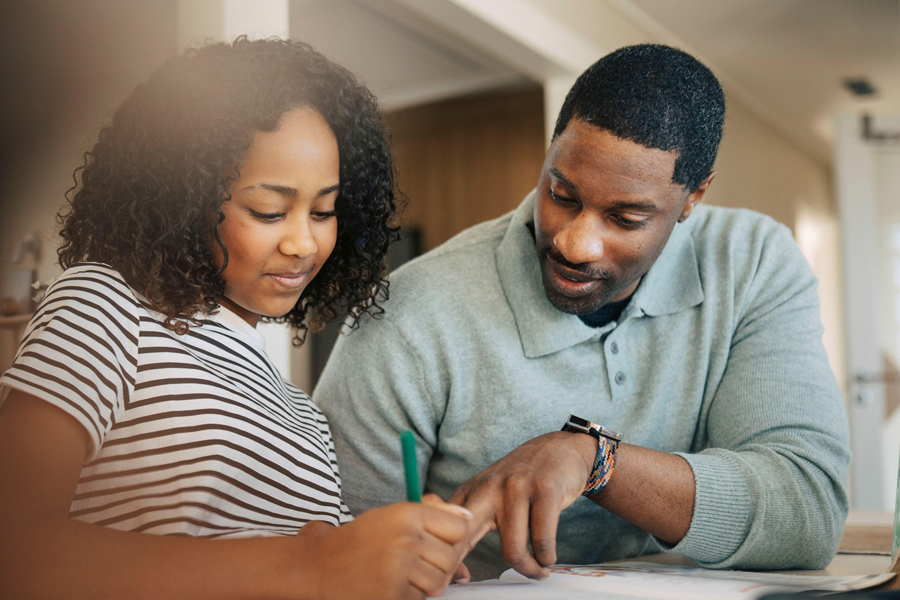 Mature man explaining lesson to daughter writing in book at home