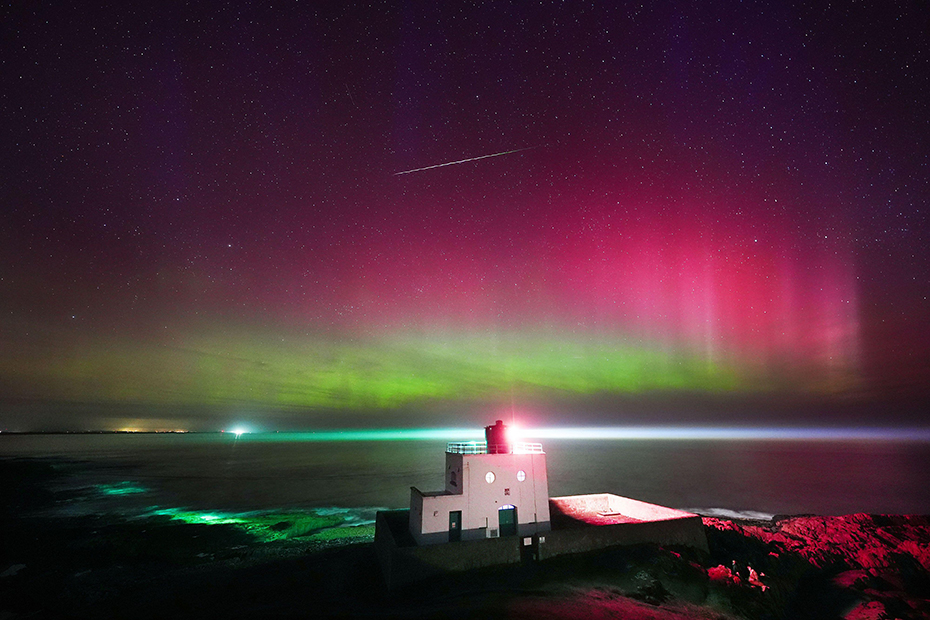 A meteor appears as the aurora borealis, commonly known as the Northern Lights, light up the skies above Bamburgh lighthouse in Northumberland