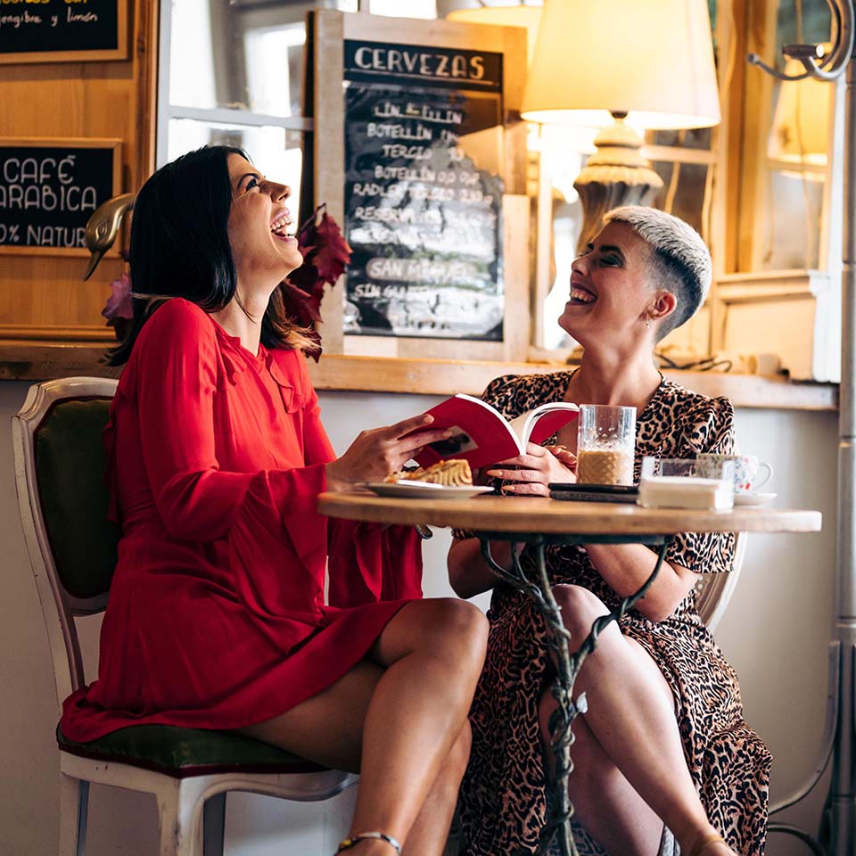 Deux amies riant et lisant un livre dans un bar moderne.